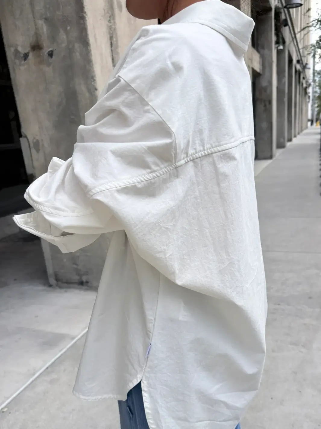 Side view of person wearing a button up 'Light Weight Owen Shirt' in 'White' from Le Bon Shoppe on a city street | Twentyseven Toronto