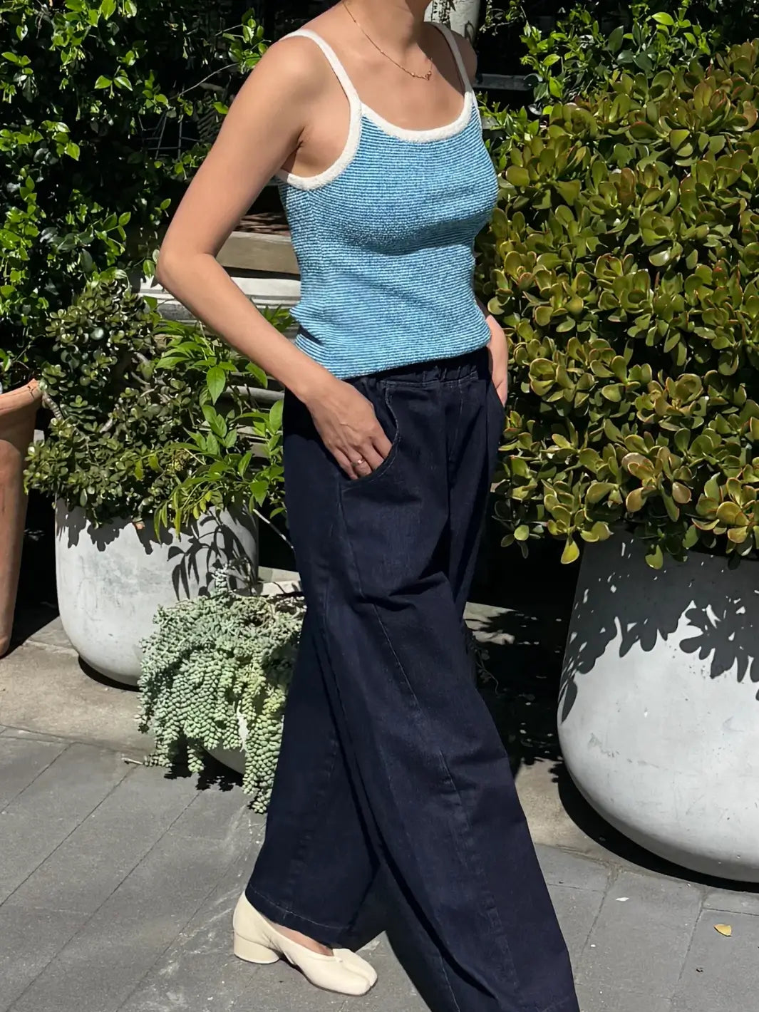 Person wearing a textured light blue 'Lily Sweater Cami' tank top in 'Blue Stripe' design with white trim from Le Bon Shoppe outside with greenery background | Twentyseven Toronto