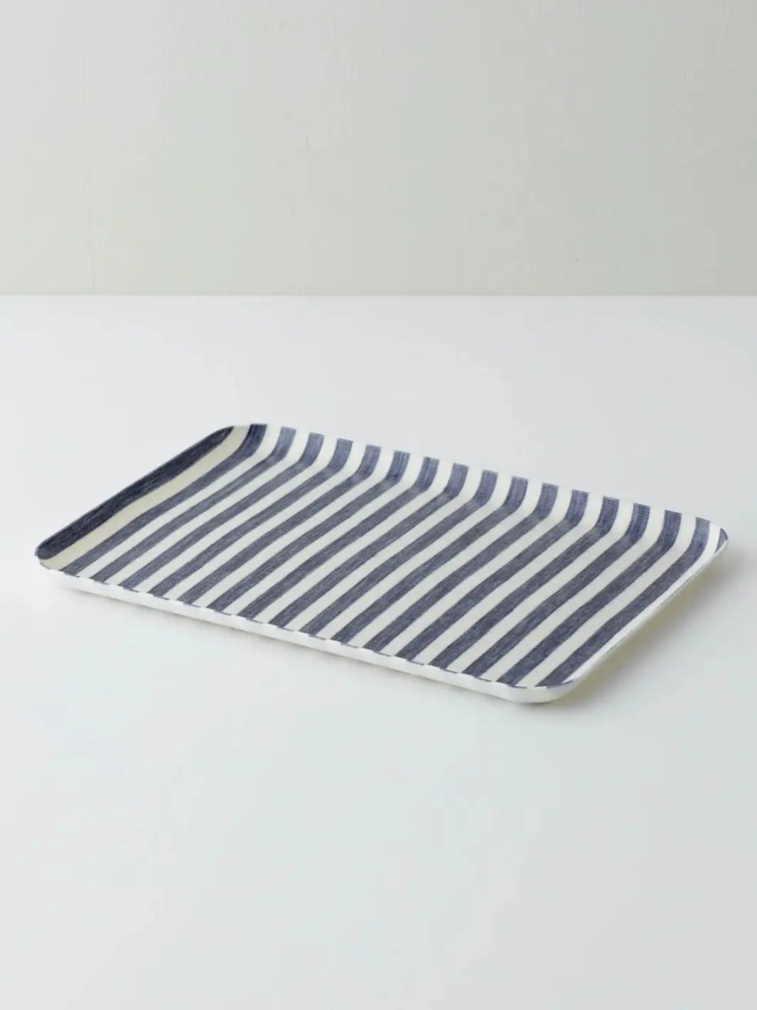 An angled studio shot of the Linen Tray (M) - White Blue Stripe from Fog Linen Work highlights its slim profile and crisp nautical pattern | Twentyseven Toronto
