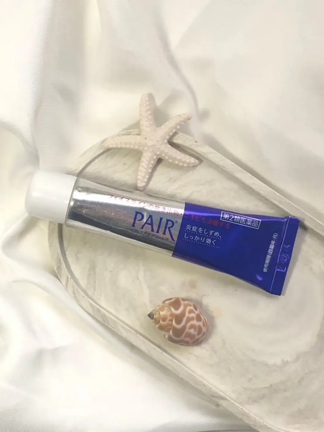 Blue and silver Lion Pair Acne Cream 24g with starfish and shell on a white background | Twentyseven Toronto