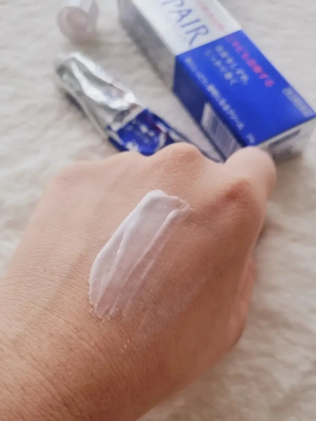 Hand with a small amount of cream applied, with a blue and silver Lion Pair Acne Cream 24g in the background | Twentyseven Toronto