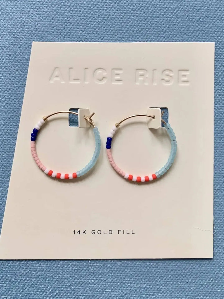 A pair of 14k gold-filled small hoop earrings featuring multicolored glass beads is displayed on a branded white product card, showing the Little Colorloop Earrings from Alice Rise Jewelry | Twentyseven Toronto