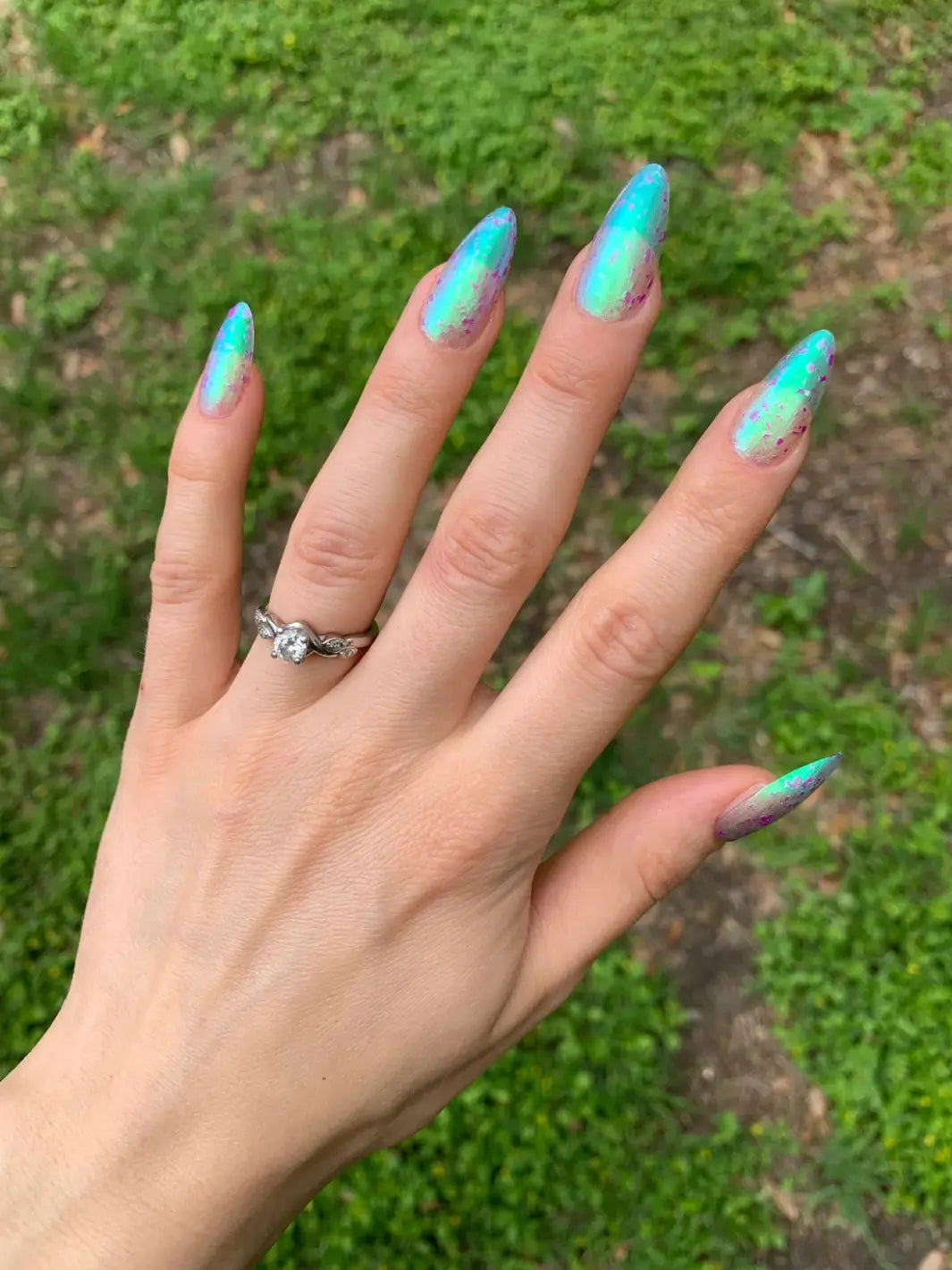 A hand over a green grassy lawn is showing off long, stiletto nails painted in Death Valley Nails Local Birds Erupting Into Hootenanny At The Spit Of Spring Sprinklers Nail Polish | Twentyseven Toronto