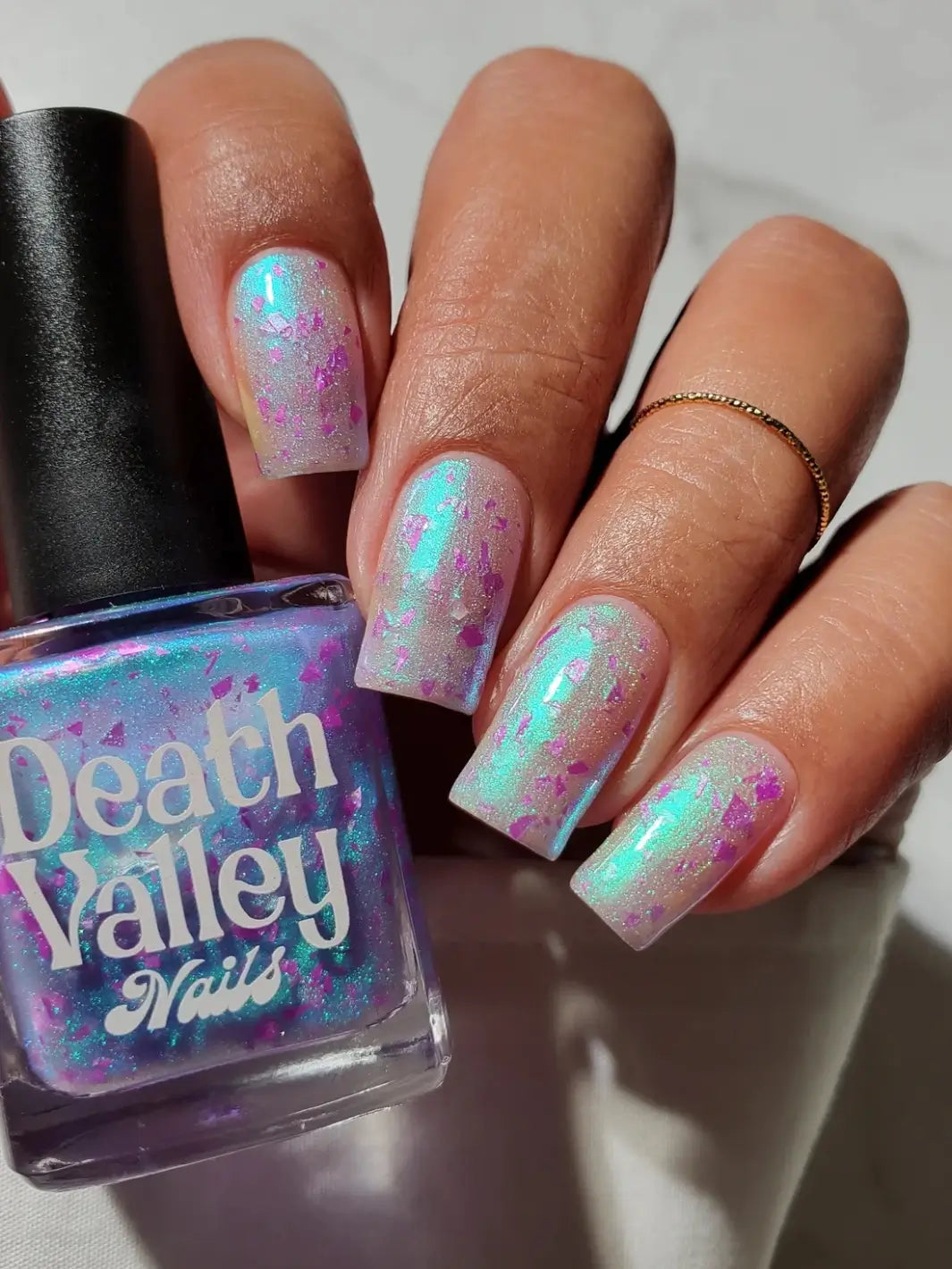 Long, square nails coated in light blue green with purple flakes Death Valley Nails Local Birds Erupting Into Hootenanny At The Spit Of Spring Sprinklers Nail Polish holding the polish bottle | Twentyseven Toronto