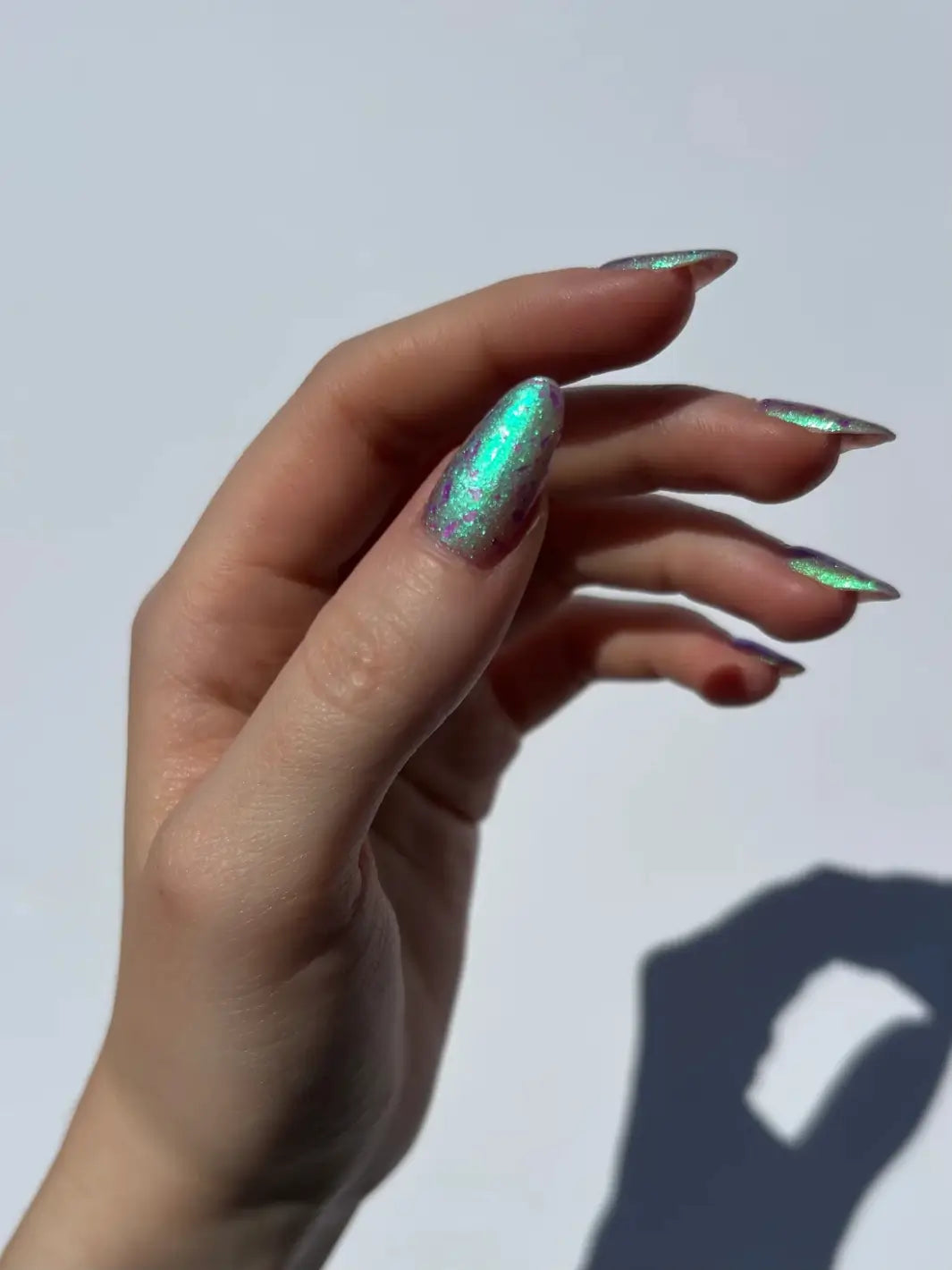 A hand displaying how Death Valley Nails Local Birds Erupting Into Hootenanny At The Spit Of Spring Sprinklers Nail Polish shifts to a bright, glowing green shimmer | Twentyseven Toronto