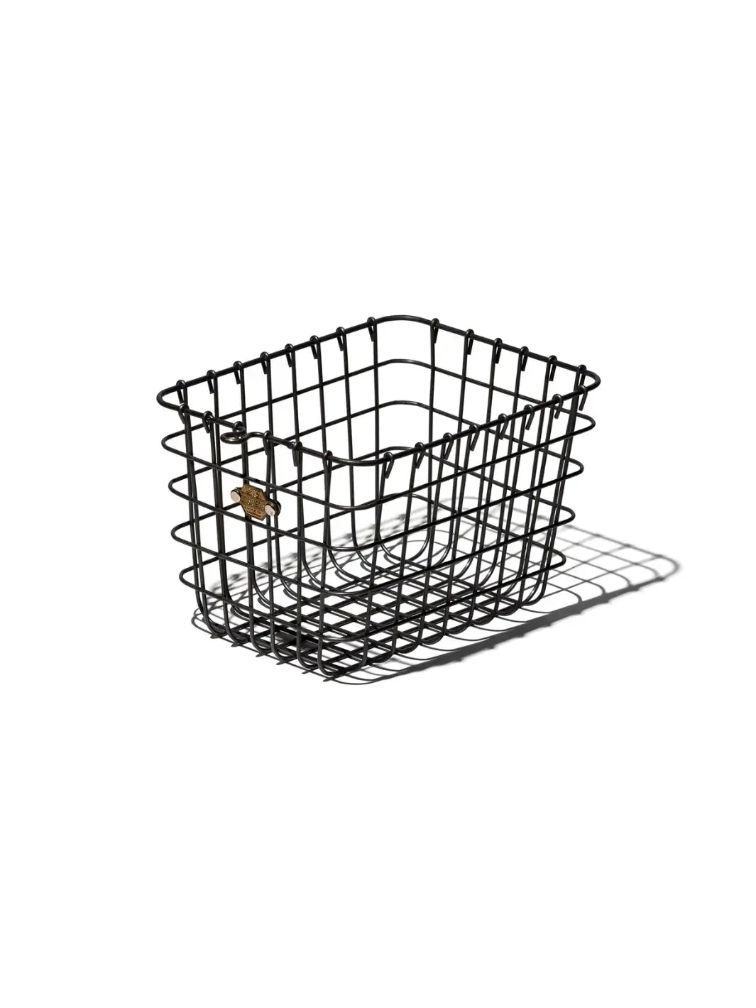 An empty Locker Basket in Medium from Puebco showcases its sturdy, dark iron grid construction, curved top loops, and a small brass numbered plate | Twentyseven Toronto