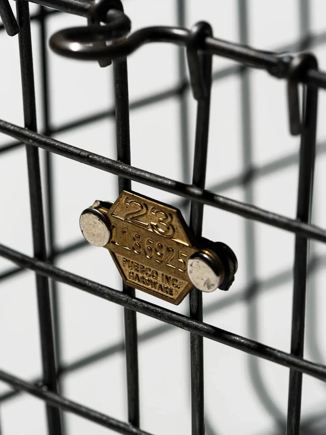 A close-up shot highlights the details and steel hardware tag attached to the wire grid of the Locker Basket - Small from Puebco | Twentyseven Toronto