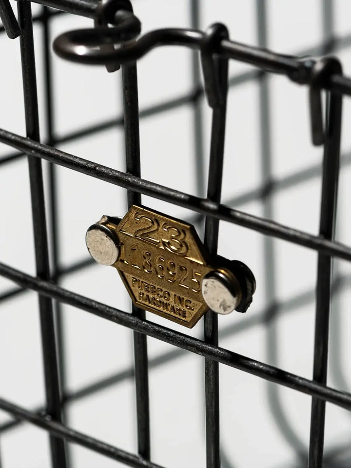 A close-up shot highlights the details and steel hardware tag attached to the wire grid of the Locker Basket - Small from Puebco | Twentyseven Toronto