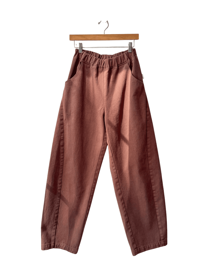 Brown 'Long Arc Pants' in 'Chocolate' from Le Bon Shoppe on a hanger against a transparent background | Twentyseven Toronto