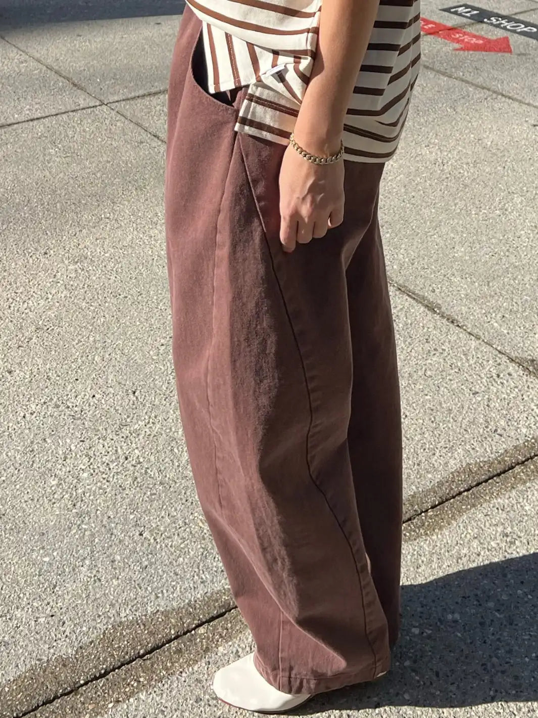 Side view image of person wearing brown wide-leg 'Long Arc Pants' in 'Chocolate' and a striped shirt from Le Bon Shoppe on a sidewalk | Twentyseven Toronto