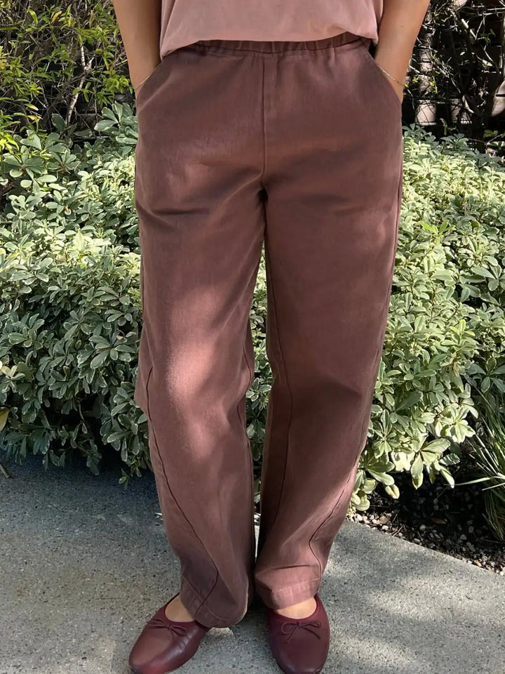 Person wearing brown 'Long Arc Pants' in 'Chocolate' from Le Bon Shoppe pants standing outdoors with greenery in the background | Twentyseven Toronto