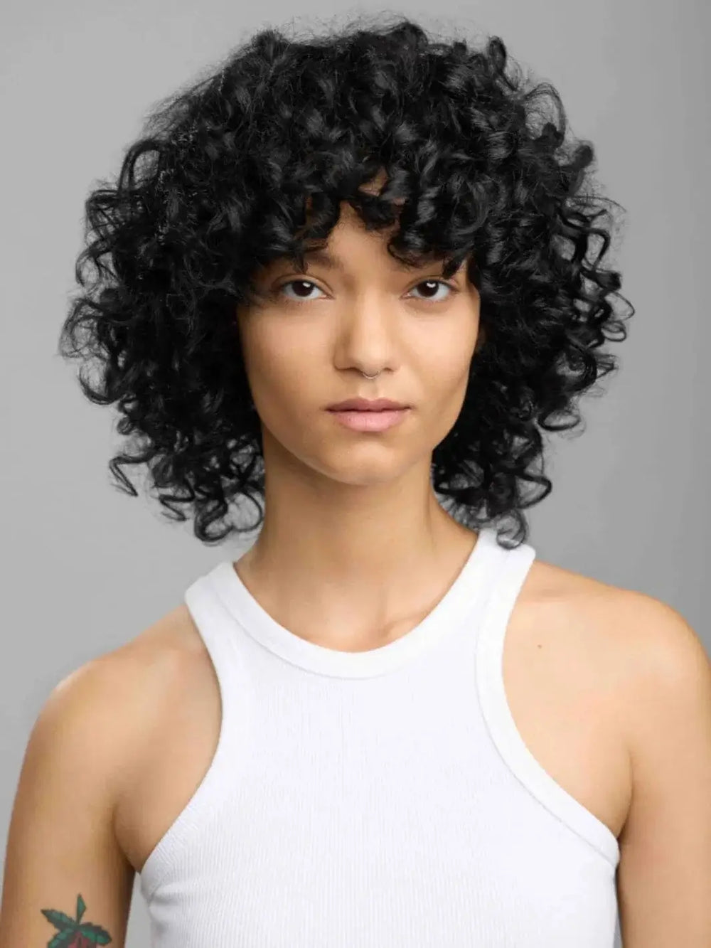 A portrait of a model showcasing defined, bouncy dark curls with a healthy shine after styling with R+Co LOST TREASURE Apple Cider Vinegar Conditioner | Twentyseven Toronto