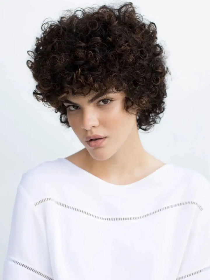 A model with voluminous, defined dark curls poses against a white background, showcasing hair cleansed and refreshed with R+Co LOST TREASURE Apple Cider Vinegar Cleansing Rinse | Twentyseven Toronto