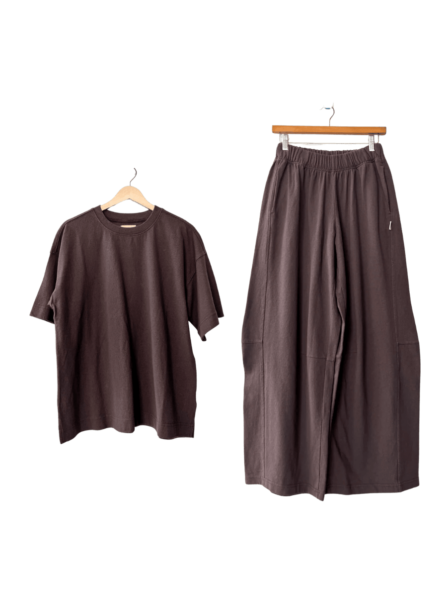 Brown Le Bon Shoppe 'Jayden Tee' t-shirt and brown wide-leg 'Bare Pants' in 'Chocolate' on hangers against a transparent background | Twentyseven Toronto