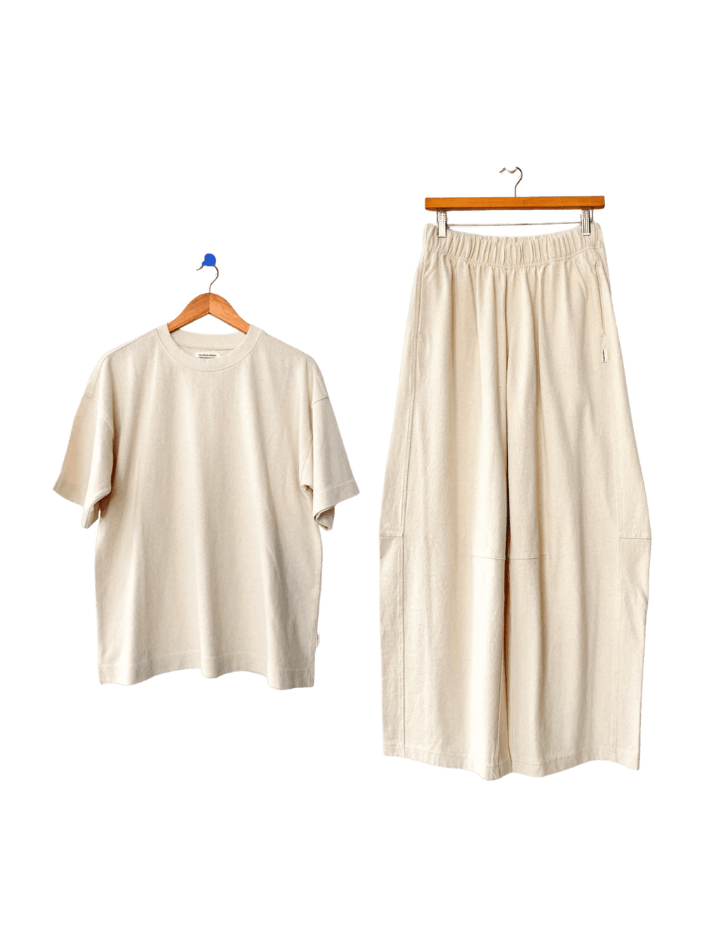 Off-white Le Bon Shoppe 'Jayden Tee' t-shirt and wide-leg 'Bare Pants' in 'Naturel' on hangers against a transparent background | Twentyseven Toronto