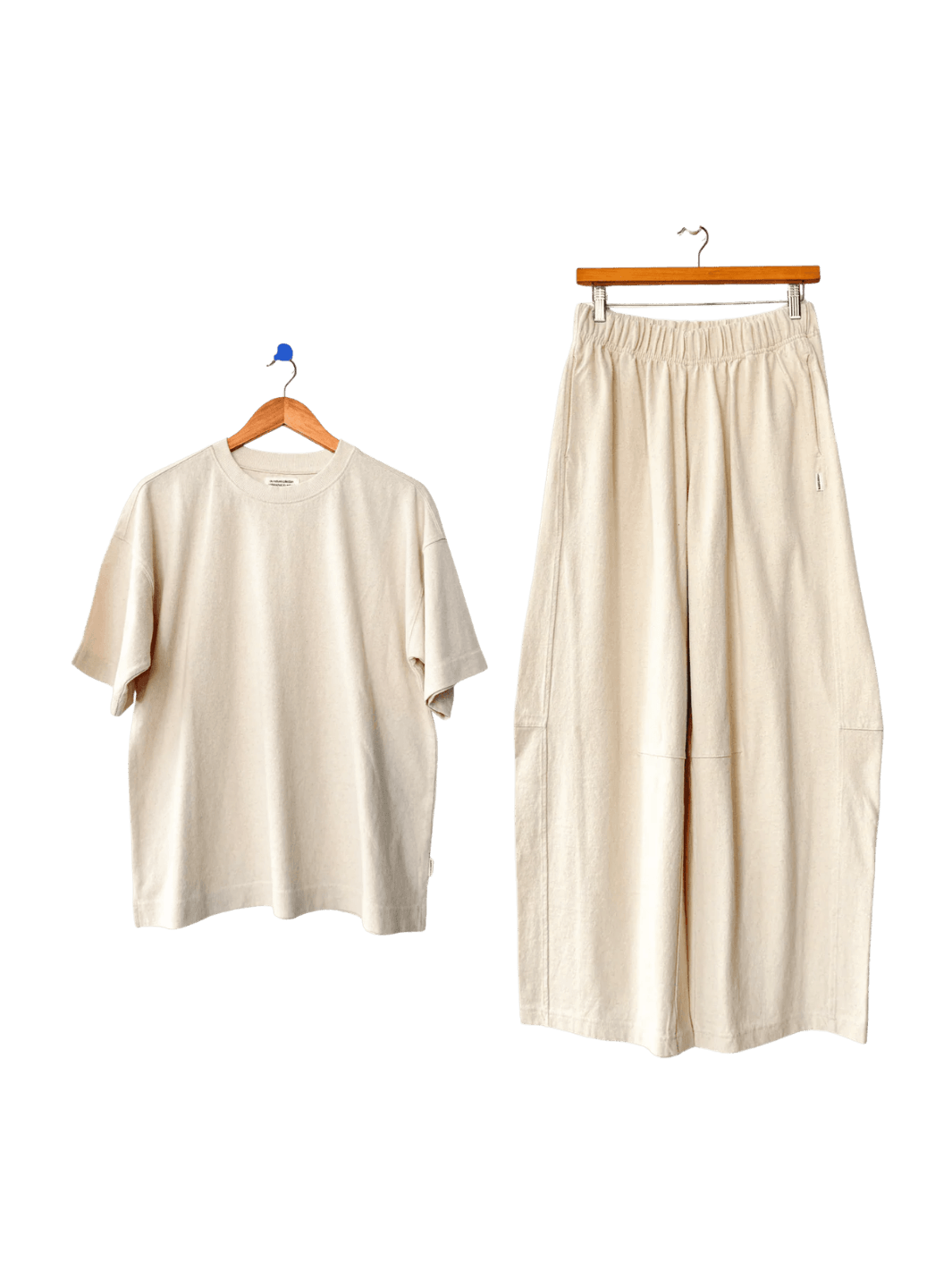 Off-white Le Bon Shoppe 'Jayden Tee' t-shirt and wide-leg 'Bare Pants' in 'Naturel' on hangers against a transparent background | Twentyseven Toronto