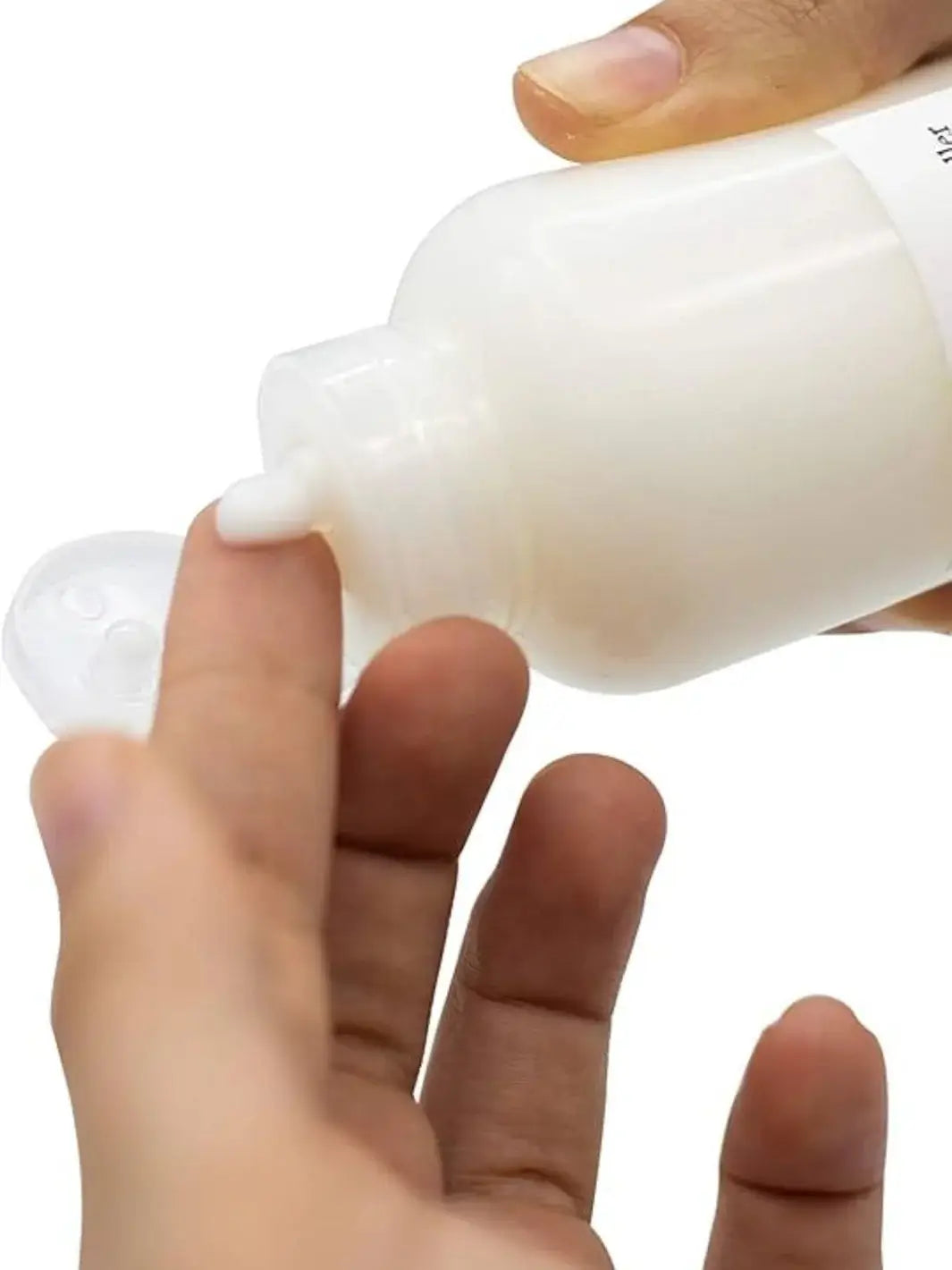 A close-up shot shows a hand squeezing a dollop of white cream product from a bottle of Davines LOVE Curl Controller onto a fingertip against a white background | Twentyseven Toronto