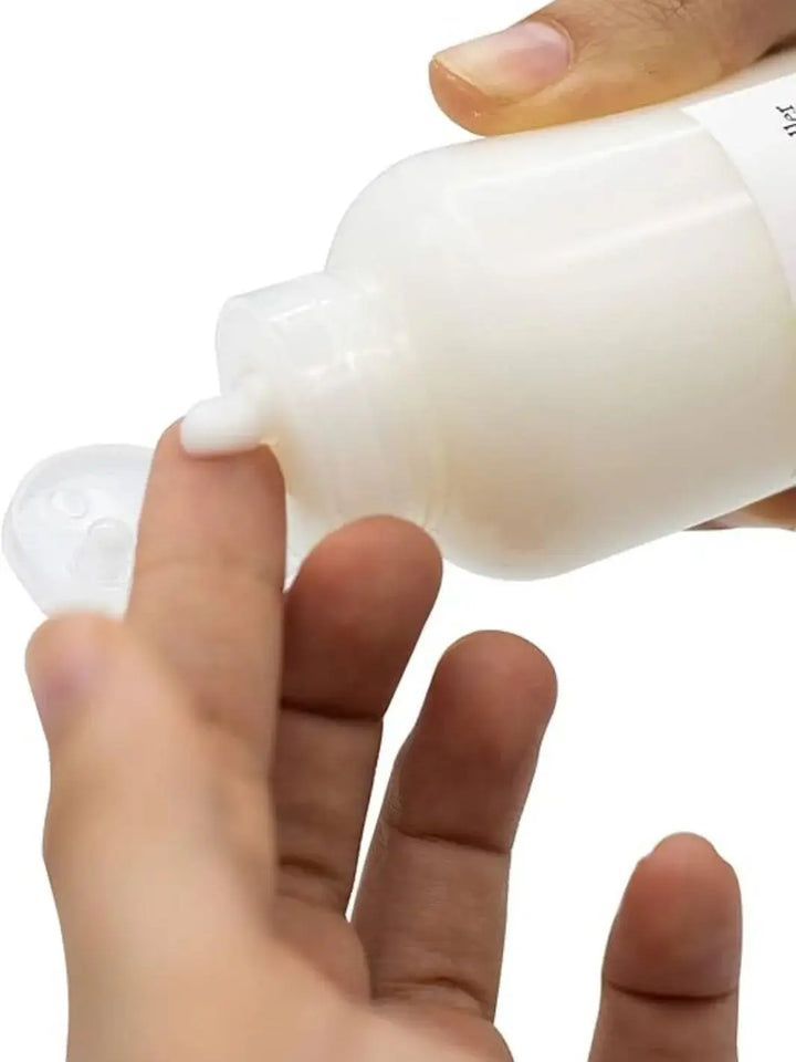 A close-up shot shows a hand squeezing a dollop of white cream product from a bottle of Davines LOVE Curl Controller onto a fingertip against a white background | Twentyseven Toronto