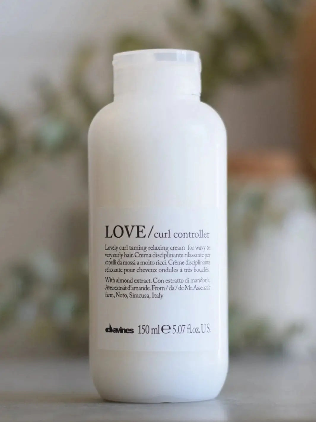 A white bottle of Davines LOVE Curl Controller stands upright against a softly blurred background | Twentyseven Toronto