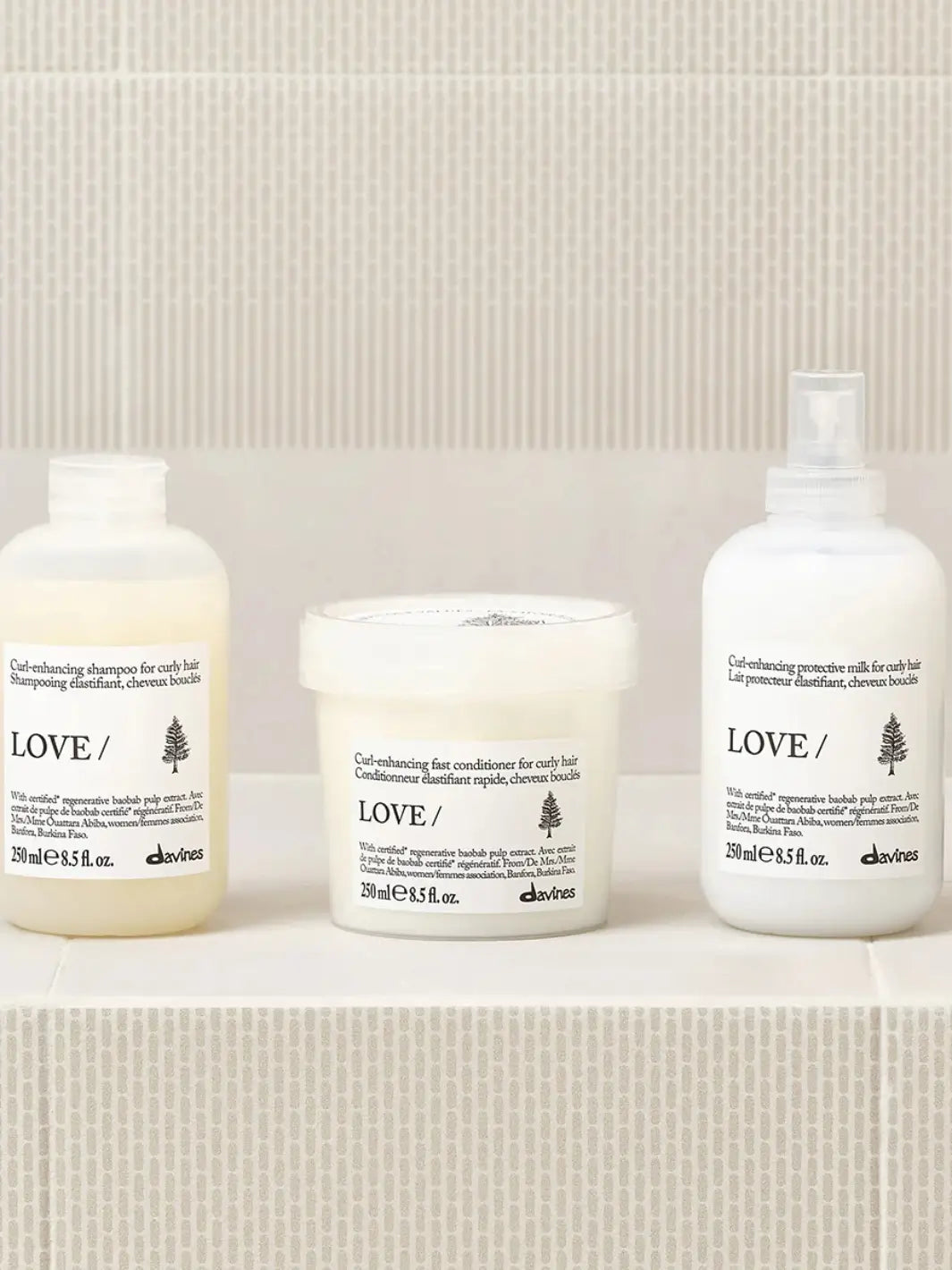 A product lineup photo shows the Davines LOVE CURL Enhancing Milk spray bottle positioned on a tiled shelf alongside its matching curl-enhancing shampoo and fast conditioner | Twentyseven Toronto