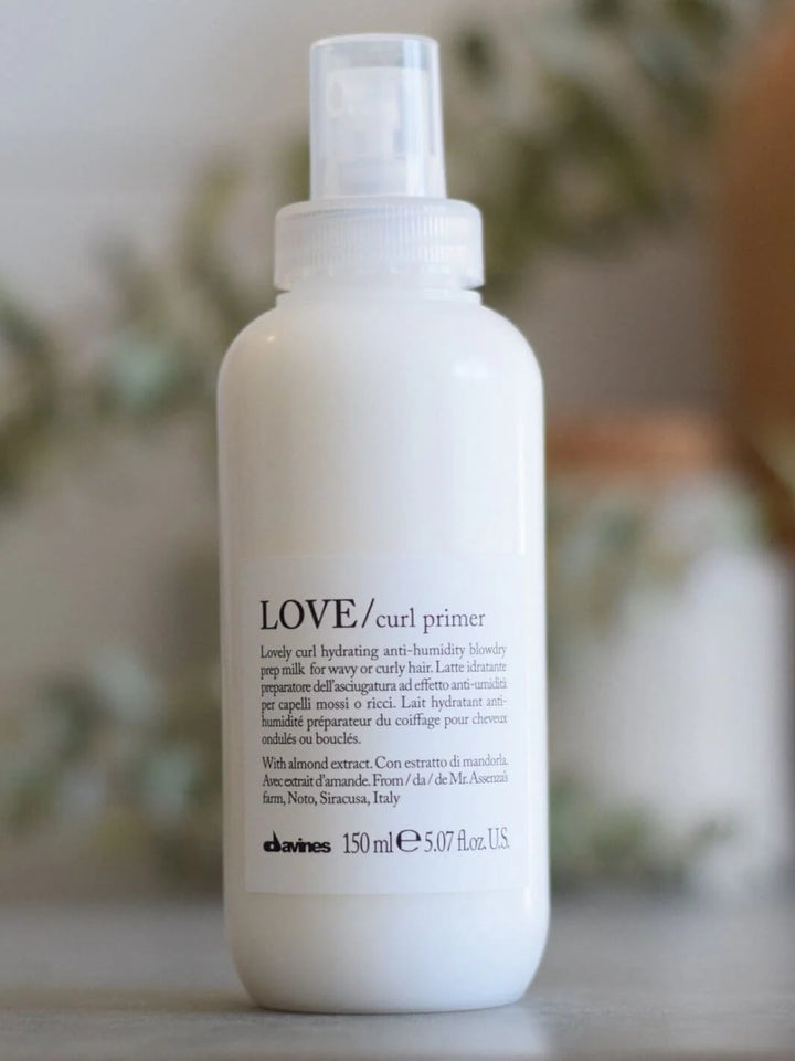 A white spray bottle of Davines LOVE Curl Primer stands upright against a blurred background | Twentyseven Toronto