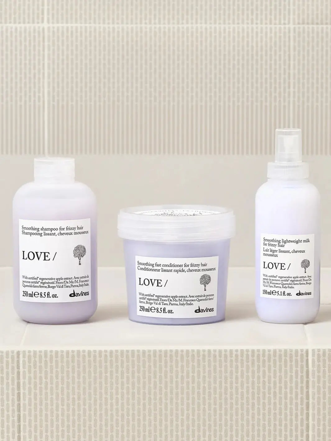 A product group shot shows the Davines LOVE SMOOTHING Lightweight Milk spray bottle resting on a white tiled surface alongside its matching smoothing shampoo and fast conditioner | Twentyse