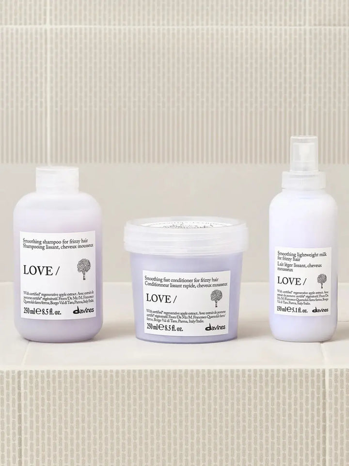 A product group shot shows the Davines LOVE SMOOTHING Lightweight Milk spray bottle resting on a white tiled surface alongside its matching smoothing shampoo and fast conditioner | Twentyse