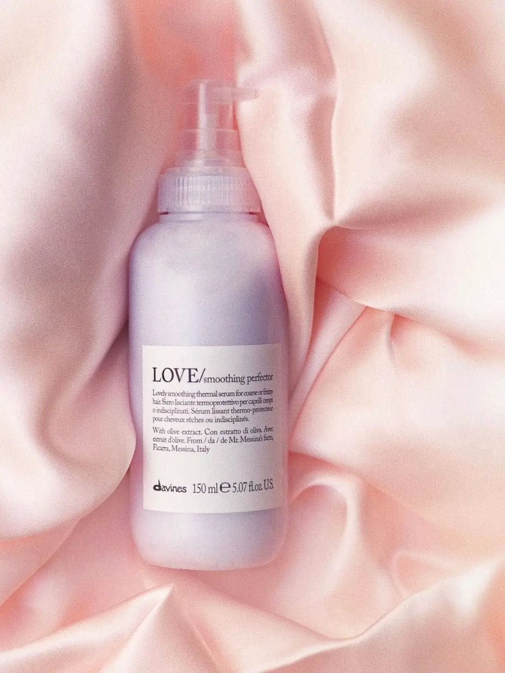 A light purple pump bottle of Davines LOVE Smoothing Perfector nestled in folds of soft, shimmering pink satin | Twentyseven Toronto