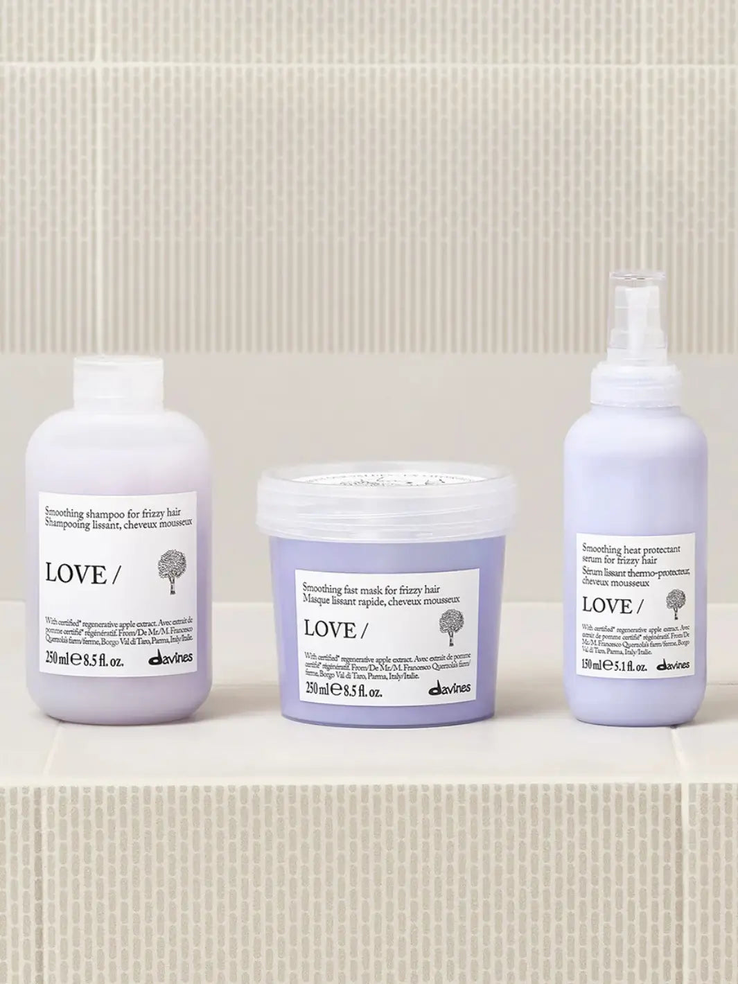 A group shot shows the Davines LOVE SMOOTHING Serum spray bottle standing on a tiled surface next to its matching smoothing shampoo and mask | Twentyseven Toronto
