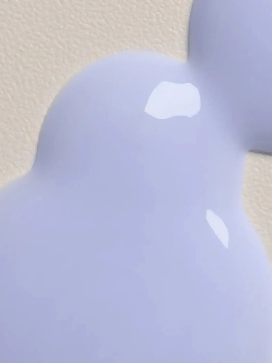 A macro close-up shot shows the smooth, glossy texture of a lavender-colored dollop of Davines LOVE SMOOTHING Serum spread across a textured beige surface.