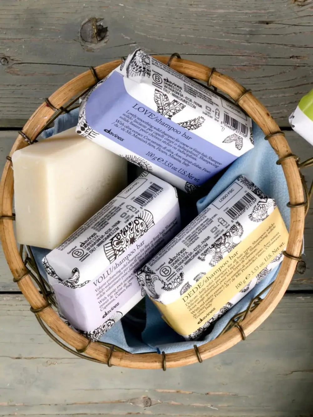 A round woven basket holds an unwrapped solid soap bar alongside several packaged items, including a wrapped Davines LOVE Smooth Shampoo Bar with light purple labeling | Twentyseven Toronto