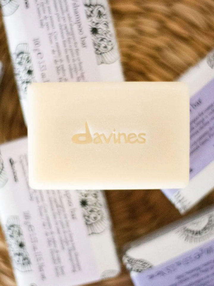 A close-up, top-down shot highlights an unwrapped Davines LOVE Smooth Shampoo Bar stamped with the brand name, surrounded by wrapped shampoo bars on a woven surface | Twentyseven Toronto