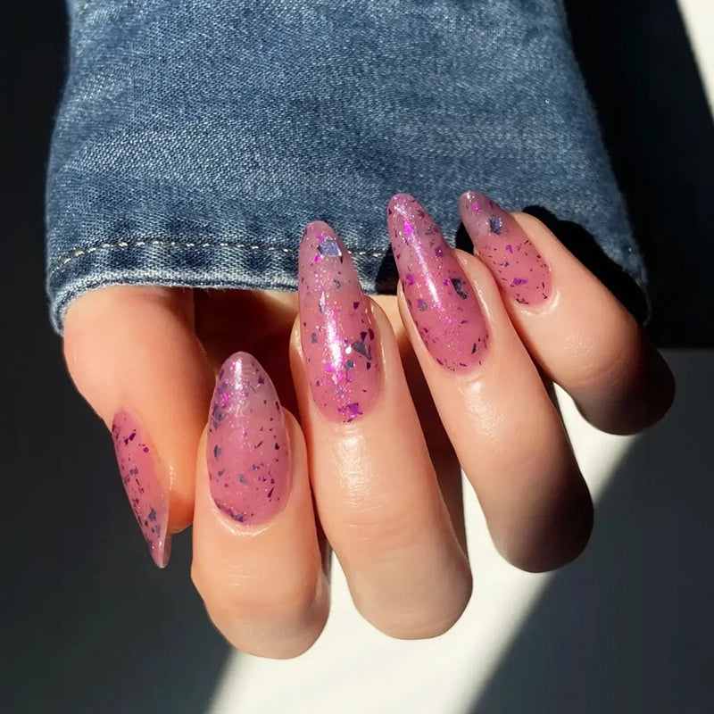 Hand with long almond-shaped nails featuring a sheer pink manicure with iridescent purple flakes in direct sunlight | Twentyseven Toronto