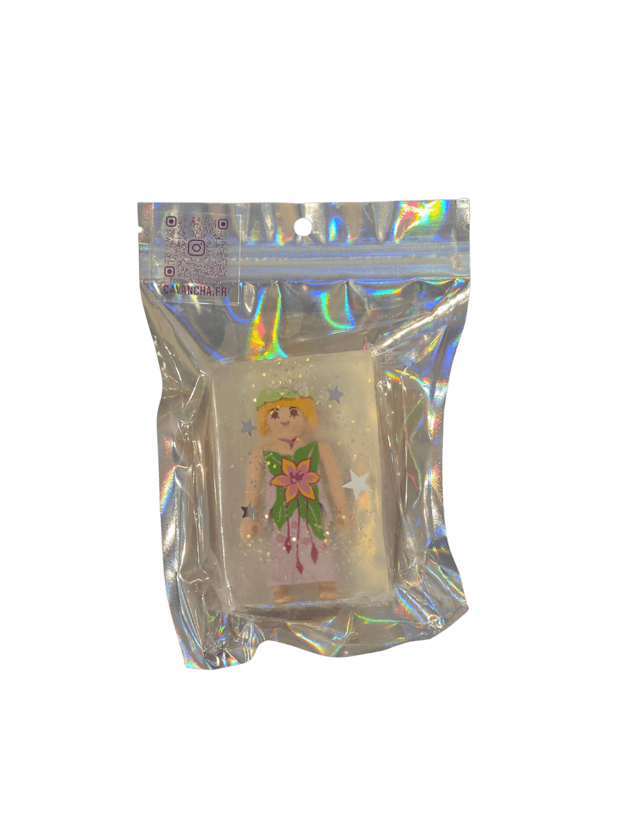 A clear bar of Cavancha Magic Glitter Soap Adults - Playmo, containing a small Playmobil-style woman figurine in a floral dress and embedded star glitter, packaged inside a shiny holographic pouch | Twentyseven Toronto