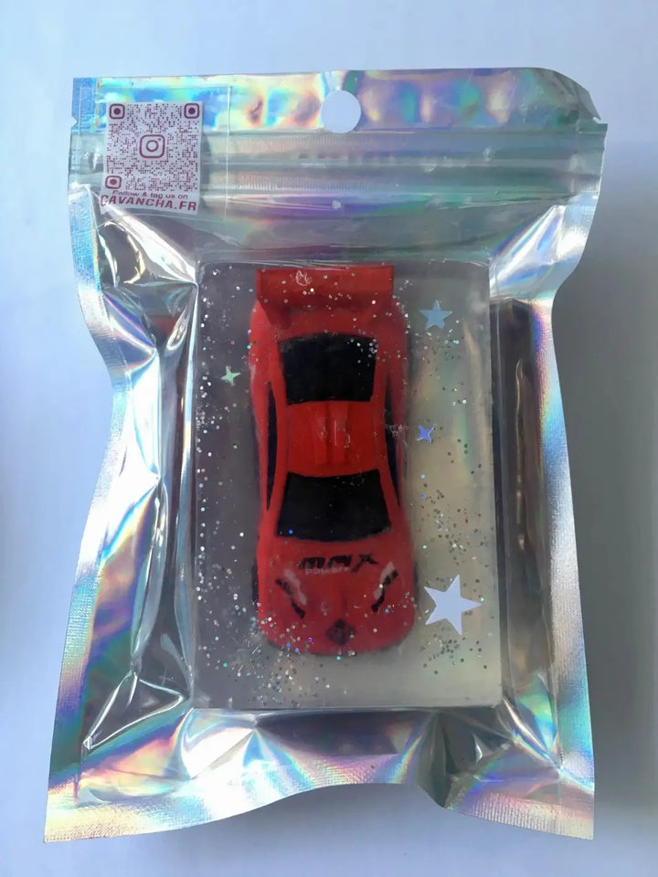 A single bar of clear Cavancha Magic Glitter Soap - Cars with an embedded red toy sports car and silver glitter star decorations, sealed in a reflective holographic pouch | Twentyseven Toronto