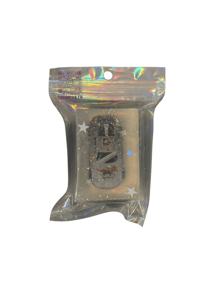 A clear bar of Cavancha Magic Glitter Soap - Cars, containing a small toy race car with dinosaur graphics embedded alongside loose star glitter, packaged inside a shiny holographic pouch | Twentyseven Toronto
