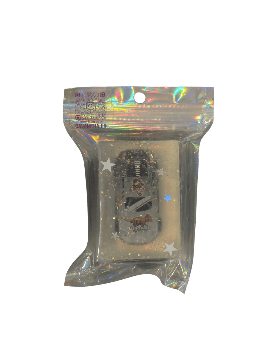 A clear bar of Cavancha Magic Glitter Soap - Cars, containing a small toy race car with dinosaur graphics embedded alongside loose star glitter, packaged inside a shiny holographic pouch | Twentyseven Toronto