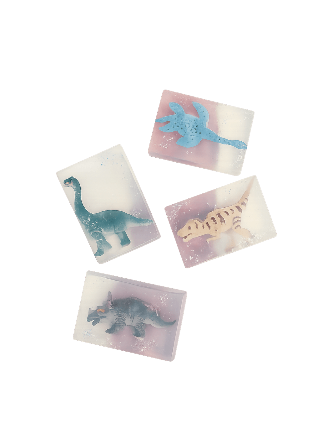 Four bars of semi-translucent Cavancha Magic Glitter Soap - Dinos are scattered against a transparent background, each embedding a different miniature dinosaur toy | Twentyseven Toronto