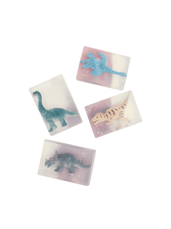 Four bars of semi-translucent Cavancha Magic Glitter Soap - Dinos are scattered against a transparent background, each embedding a different miniature dinosaur toy | Twentyseven Toronto
