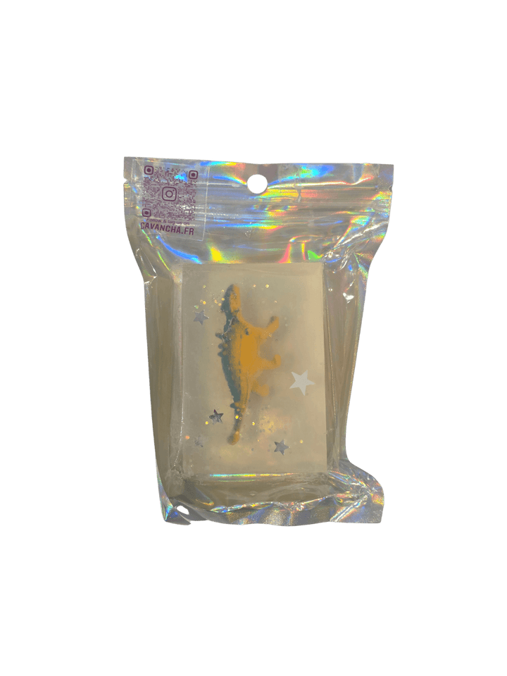 A clear bar of Cavancha Magic Glitter Soap - Dinos, containing a small yellow dinosaur figurine and embedded star glitter, packaged inside a shiny holographic pouch | Twentyseven Toronto