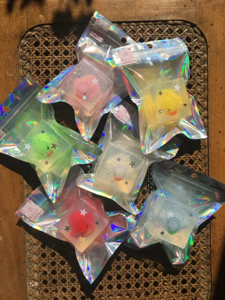 Six individually packaged cube bars of Cavancha Magic Glitter Soap - Ducky containing various colorful duck toys and star glitter are arranged together on a woven surface | Twentyseven Toronto