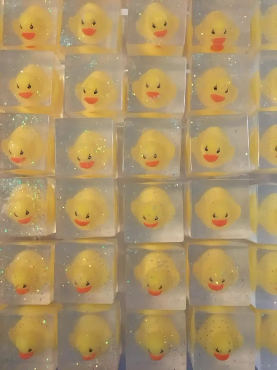 A grid arrangement highlights multiple clear, square bars of Cavancha Magic Glitter Soap - Ducky, each containing an identical classic yellow rubber duck surrounded by fine glitter | Twentyseven Toronto