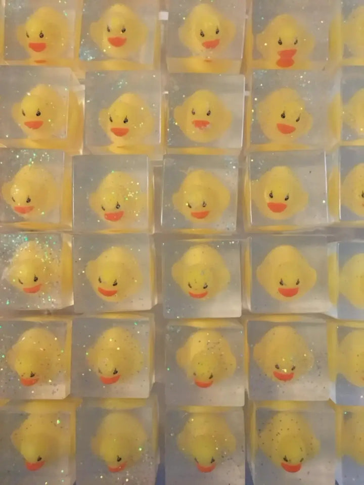 A grid arrangement highlights multiple clear, square bars of Cavancha Magic Glitter Soap - Ducky, each containing an identical classic yellow rubber duck surrounded by fine glitter | Twentyseven Toronto