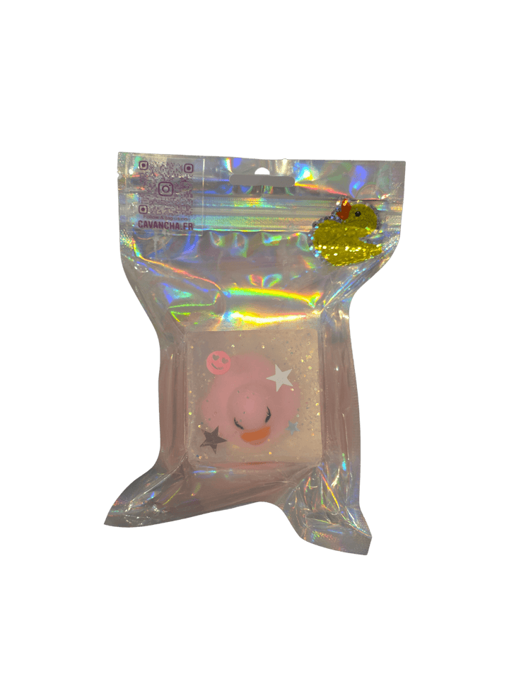 A clear bar of Cavancha Magic Glitter Soap - Ducky, embedded with a small pink duck charm, star glitter, and a tiny smiley face, packaged inside a shiny holographic pouch | Twentyseven Toronto