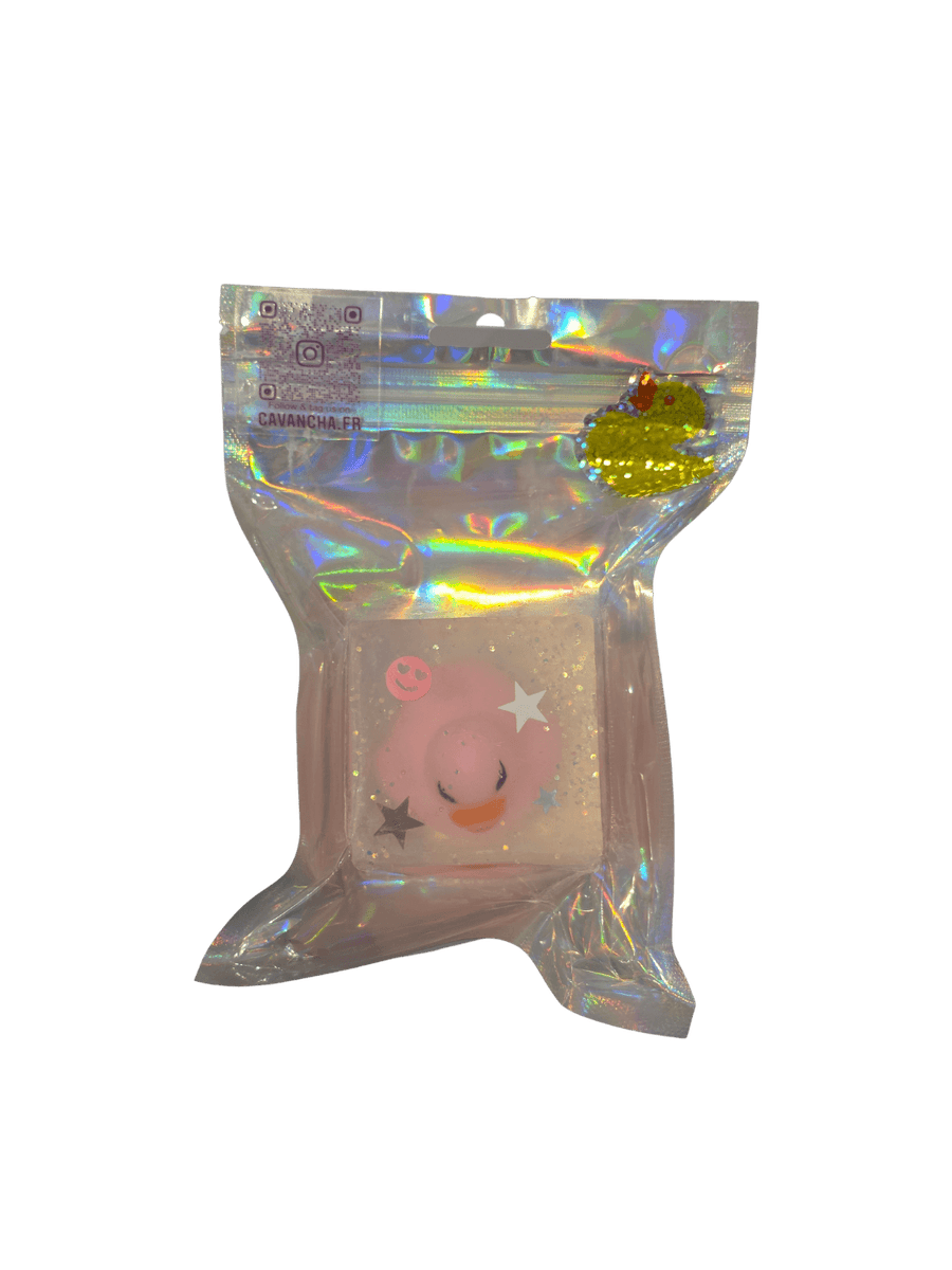 A clear bar of Cavancha Magic Glitter Soap - Ducky, embedded with a small pink duck charm, star glitter, and a tiny smiley face, packaged inside a shiny holographic pouch | Twentyseven Toronto