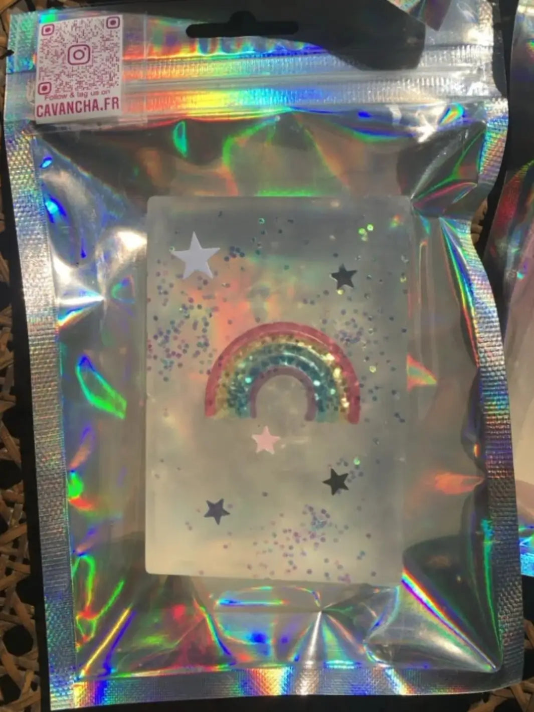 A clear bar of Cavancha Magic Glitter Soap - Fairy Tales featuring an embedded rainbow toy and loose star confetti is presented inside a reflective holographic pouch | Twentyseven Toronto