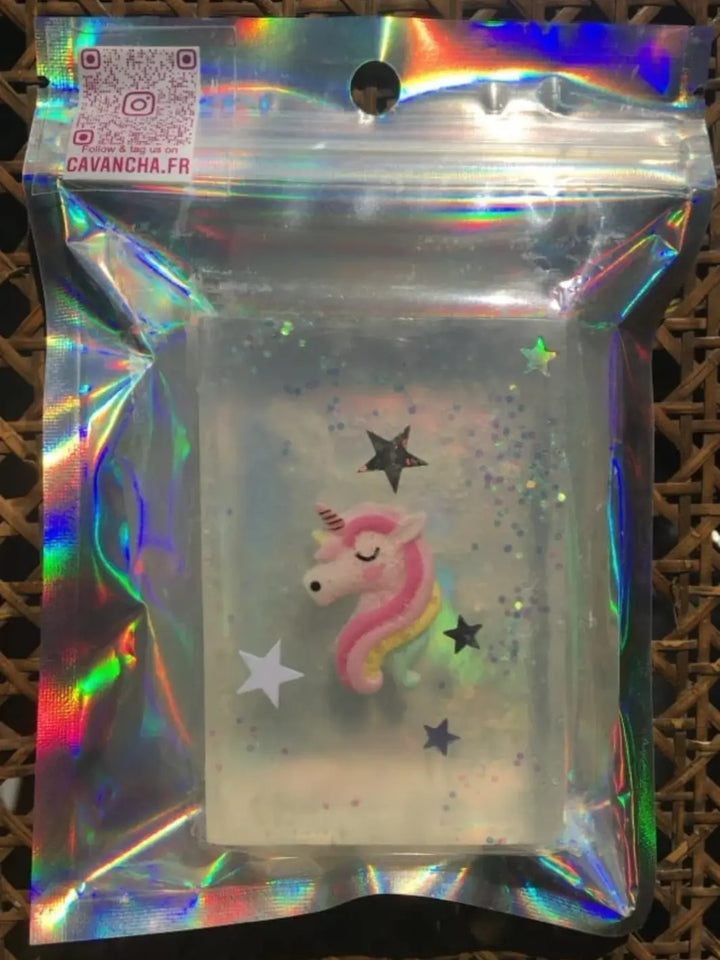 A sealed holographic pouch contains a transparent bar of Cavancha Magic Glitter Soap - Fairy Tales with an embedded pastel pink unicorn head surrounded by star shapes | Twentyseven Toronto