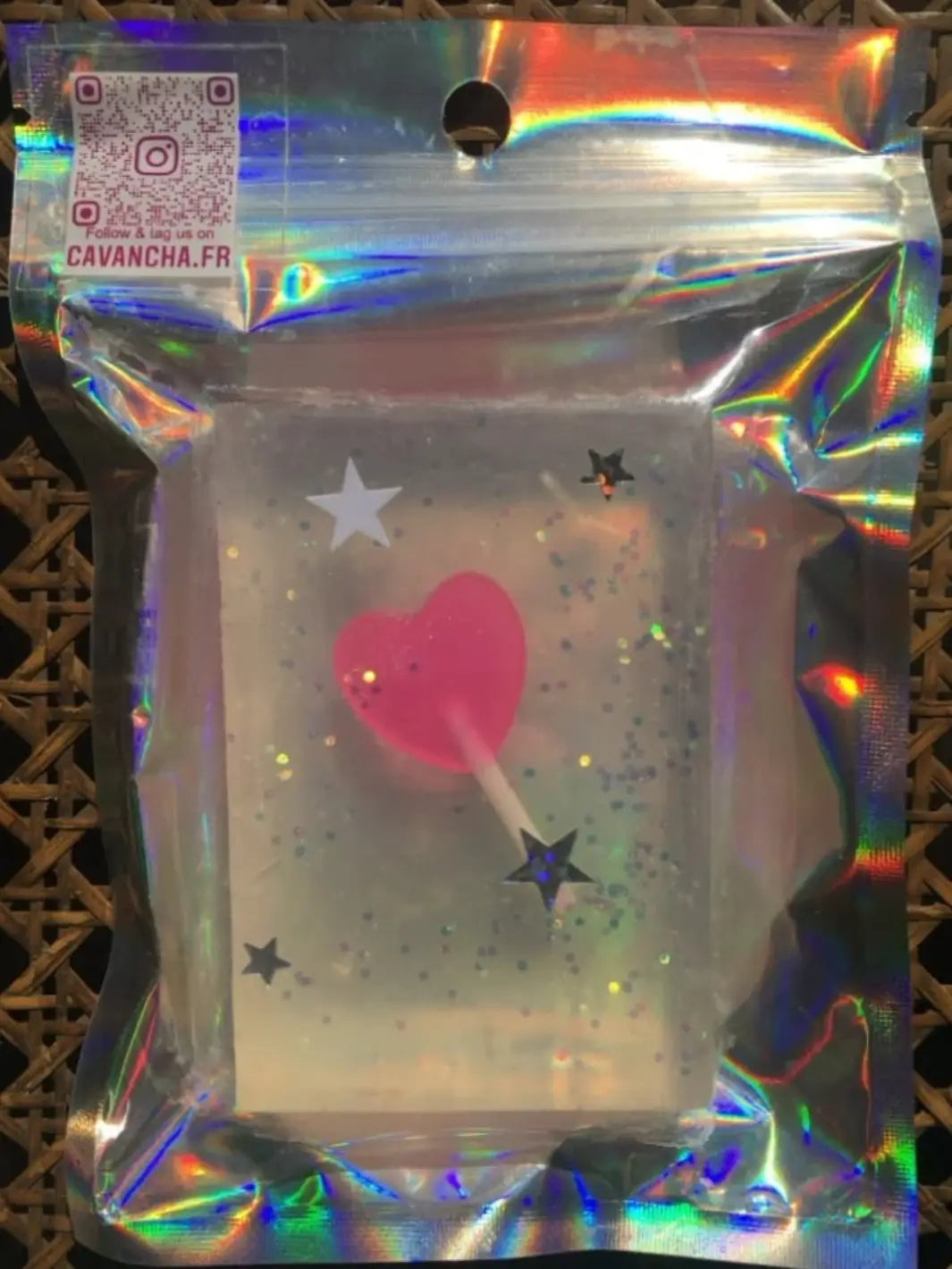 A clear bar of Cavancha Magic Glitter Soap - Fairy Tales containing an embedded bright pink heart-shaped lollipop toy is shown inside a protective holographic plastic package | Twentyseven Toronto