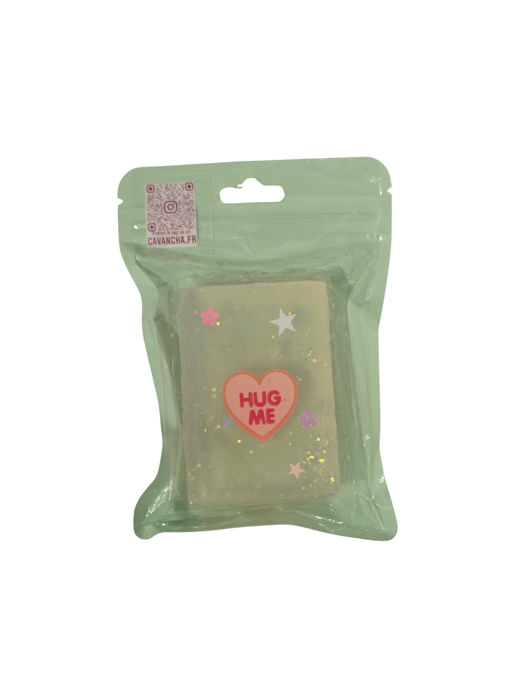 A clear bar of Cavancha Magic Glitter Soap - Fairy Tales, embedded with a pink conversation heart charm that says "HUG ME," loose glitter, and tiny star and flower accents, packaged inside a light green pouch | Twentyseven Toronto