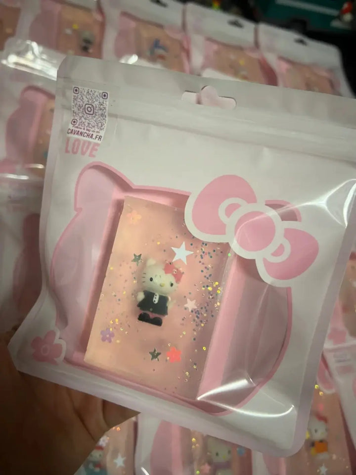 A hand holds up a packaged bar of Cavancha Magic Glitter Soap - Hello Kitty featuring a toy figure in a black outfit, with more identical pink packages blurred in the background | Twentyseven Toronto